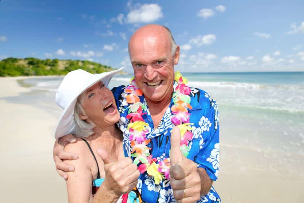 un couple de personnes âgées rit aux éclats et prendre la pose devant une plage paridisiaque