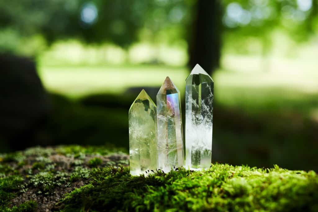 Trois cristaux de quartz clair posés sur une mousse verte sur un fond de nature.