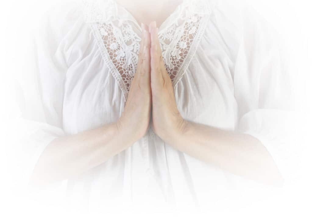 Les mains jointes en prière d'une femme habillée avec un haut en blanc.