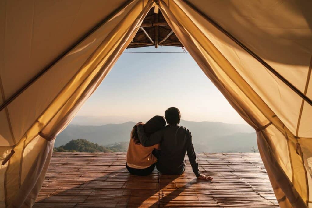 couple d'un homme et d'une femme, assis dans une grande tente contemplant tous les deux l'horizon composé de vallées verdoyantes