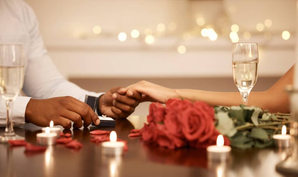 deux mains d'amoureux qui se tiennent sur une table parsemée de roses rouges et de bougies.