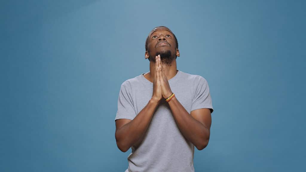 Un jeune homme joignant les mains en prière, les yeux tournés en haut.