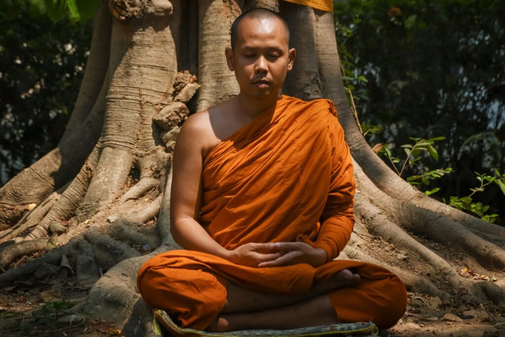 un moine bouddhiste assis devant un arbre en pleine méditation.
