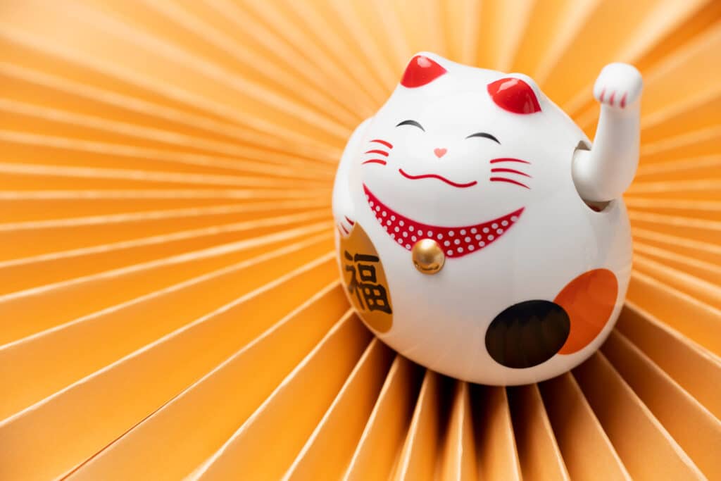 chat porte bonheur maneki-neko souriant posé sur un papier beige
