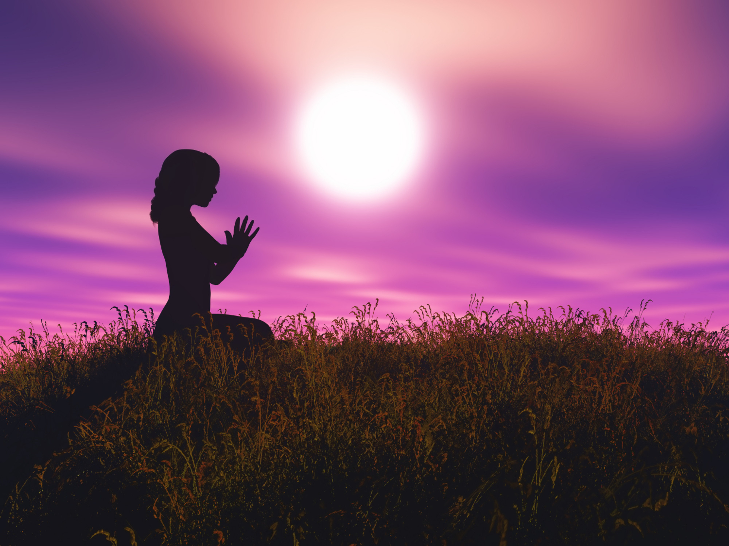 silhouette d'une femme agenouillée dans l'herbe devant un coucher de soleil