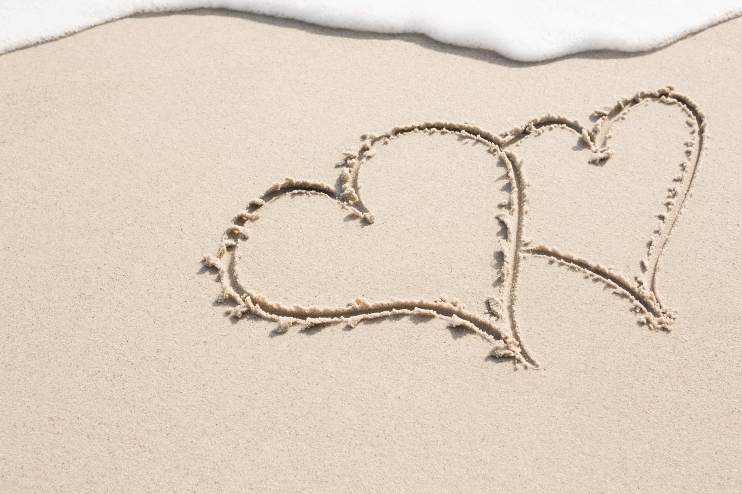 deux cœurs tracés dans le sable beige