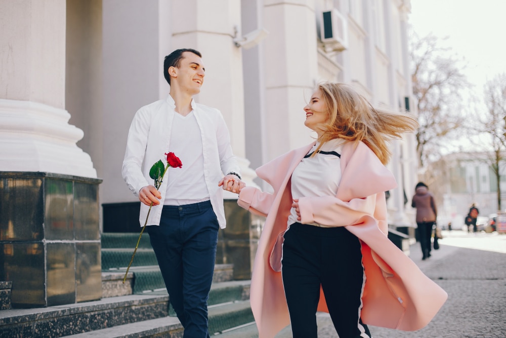un couple avec un homme qui tient une rose rouge dans la main qui se tient la main dans la rue